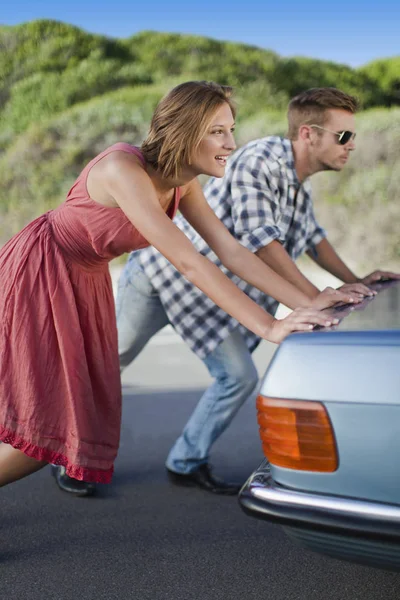 Couple pushing broken down car — Stock Photo, Image
