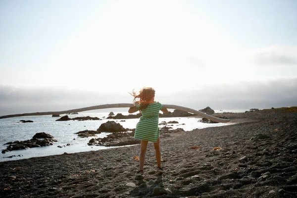 Menina com madeira à deriva em pé na praia — Fotografia de Stock