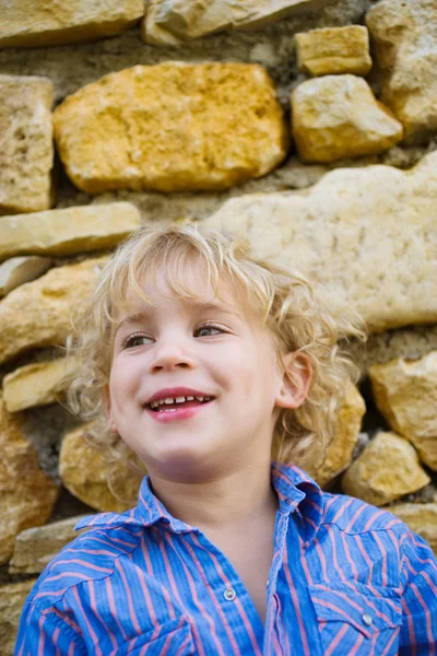 少年は笑みを浮かべて石の壁のそばに立って — ストック写真