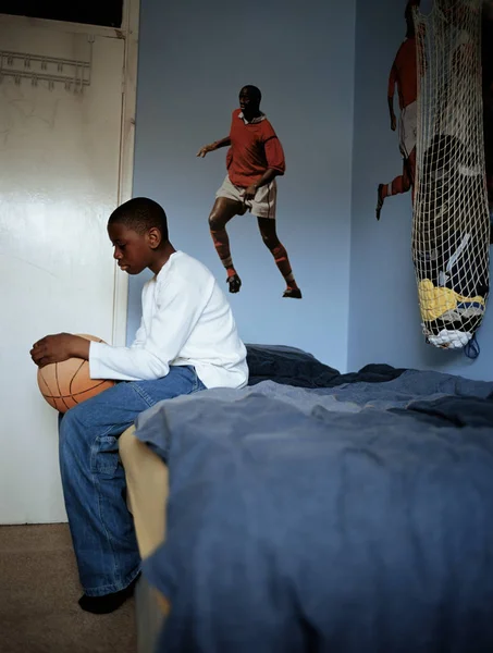 Menino segurando basquete sentado na cama — Fotografia de Stock