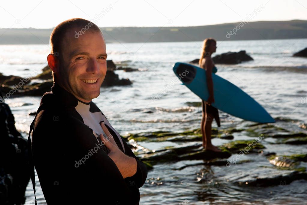 Man standing and smiling with woman holding surfboard