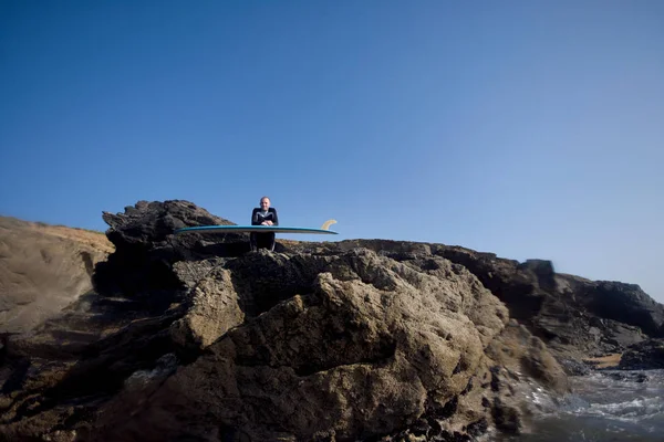 Человек, сидящий с доской для серфинга — стоковое фото