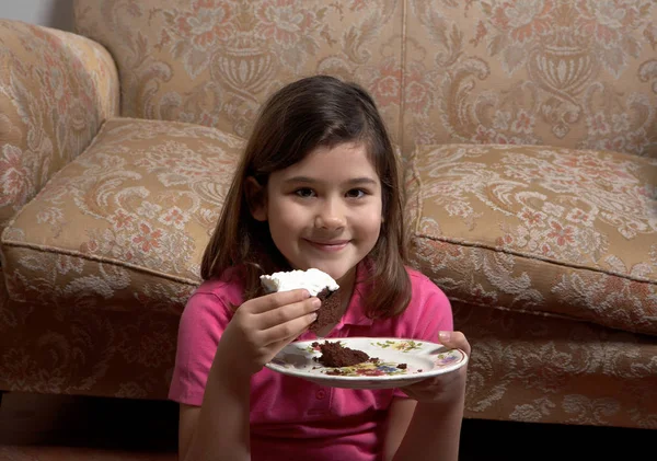 Fille assise par canapé et manger du gâteau — Photo