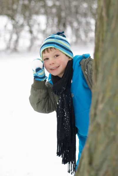 小男孩用雪球在树后面躲 — 图库照片