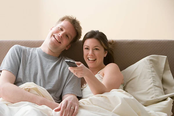 Couple with remote control laying in bed — Stock Photo, Image