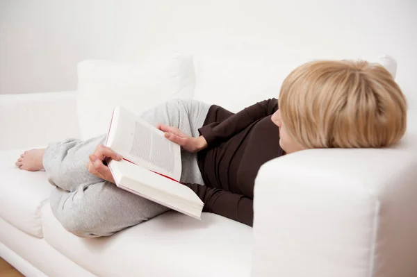 Vrouw lezen boek liggend op de Bank — Stockfoto