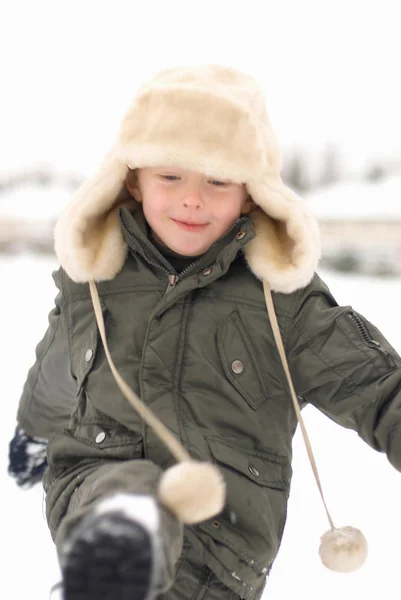 Niño en sombrero peludo pateando nieve —  Fotos de Stock