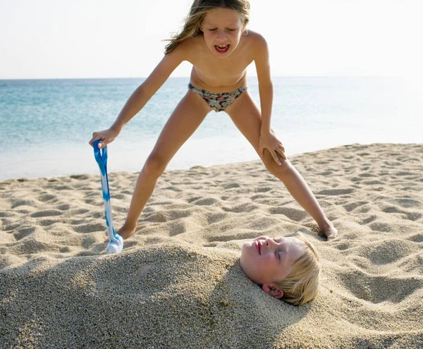 Mädchen begräbt Jungen im Sand — Stockfoto