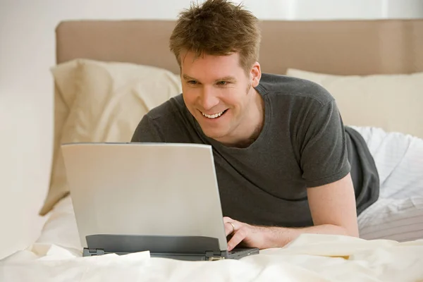 Man met laptop op bed — Stockfoto