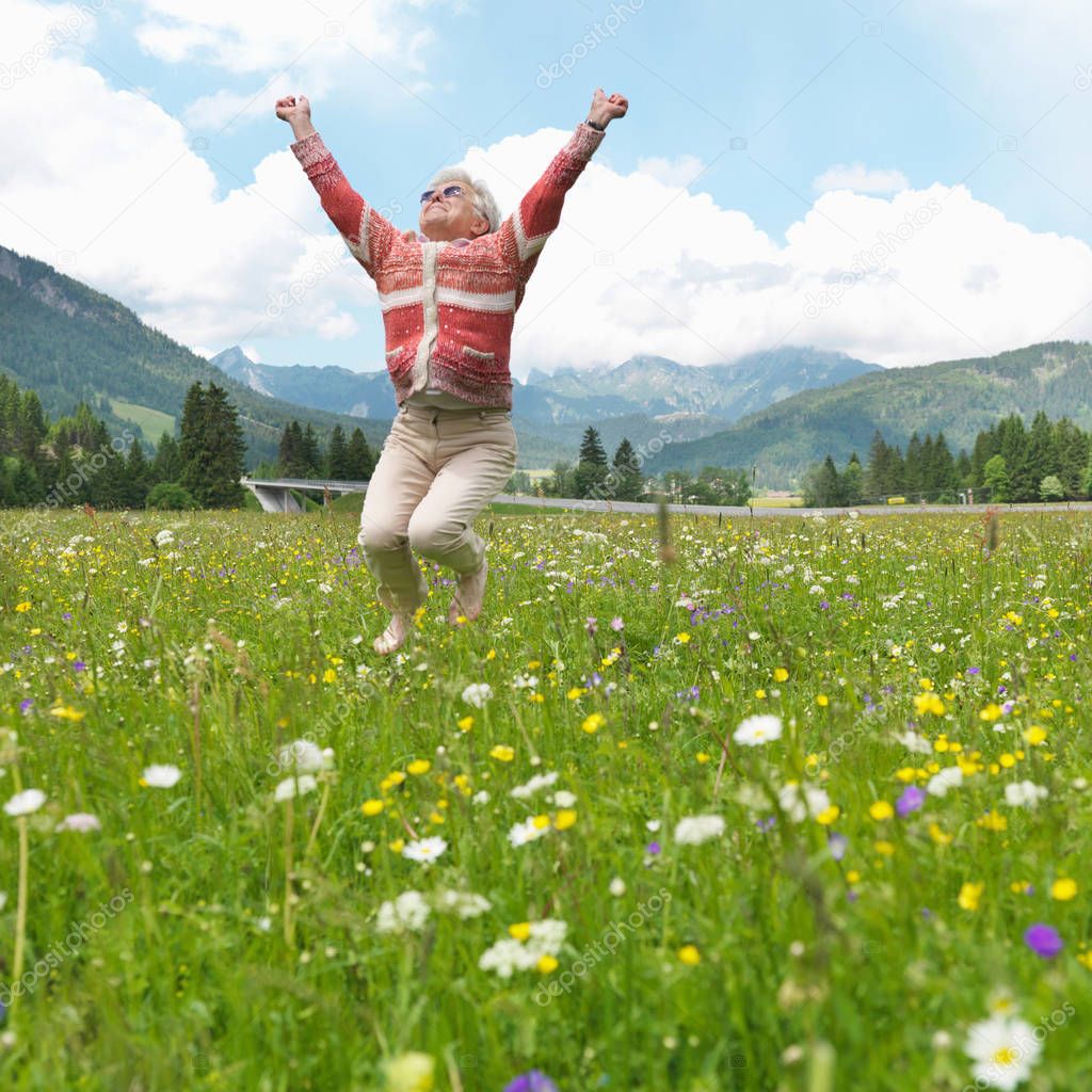 Senior woman leaping in field of flowers