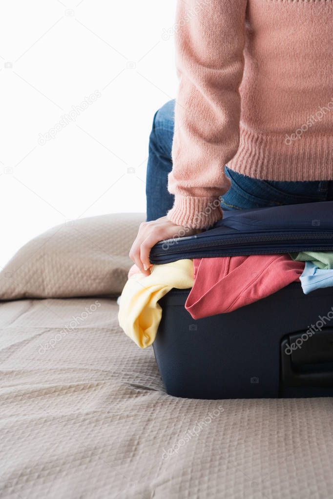 Cropped image of woman sitting on suitcase full of clothes