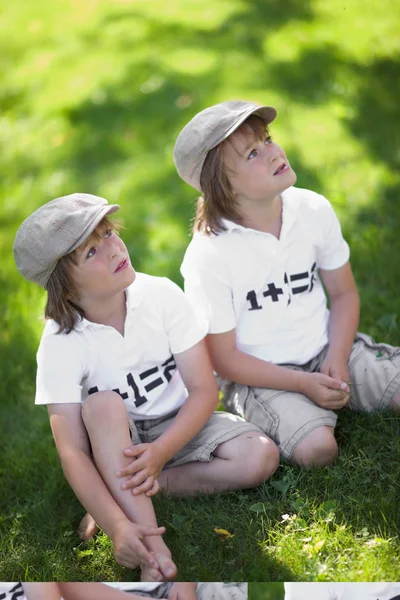 Siedząc na trawie w koszulkach identyczne bliźniaki — Zdjęcie stockowe