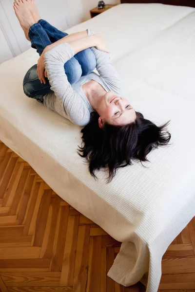 Женщина в позе эмбриона лежит на кровати — стоковое фото