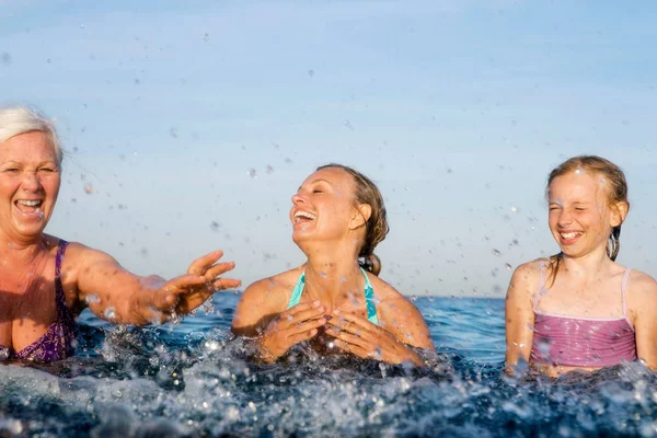 happy family with grandmother, mother and daughter having fun in water at lake