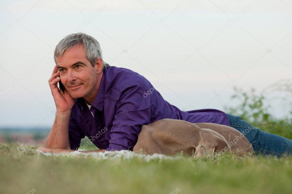 man lying with dog and speaking on phone in grass