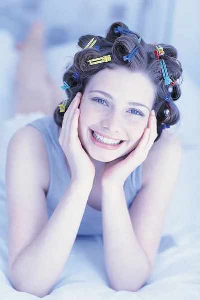 Smiling Woman with hairpins lying on bed — Stock Photo, Image