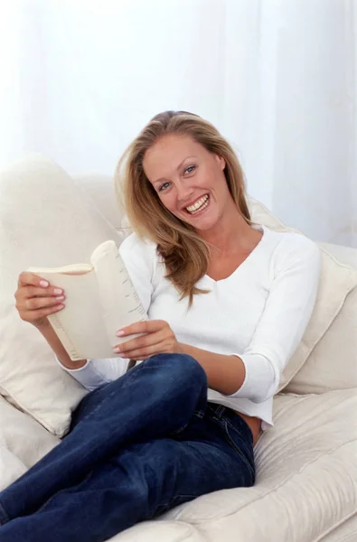 Uśmiechnięta kobieta siedzi na kanapie z książki — Zdjęcie stockowe