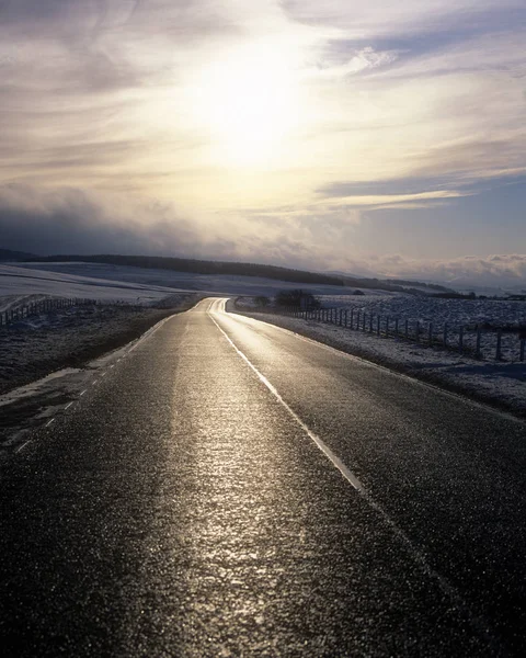 Landelijke Weg Tussen Besneeuwde Velden Met Zon Bewolkte Hemel Achtergrond — Stockfoto