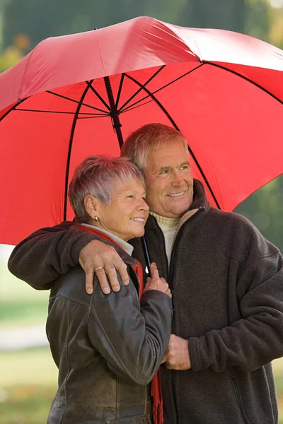 Senior Couple Using Red Umbrella Looking Away — Stock Photo, Image