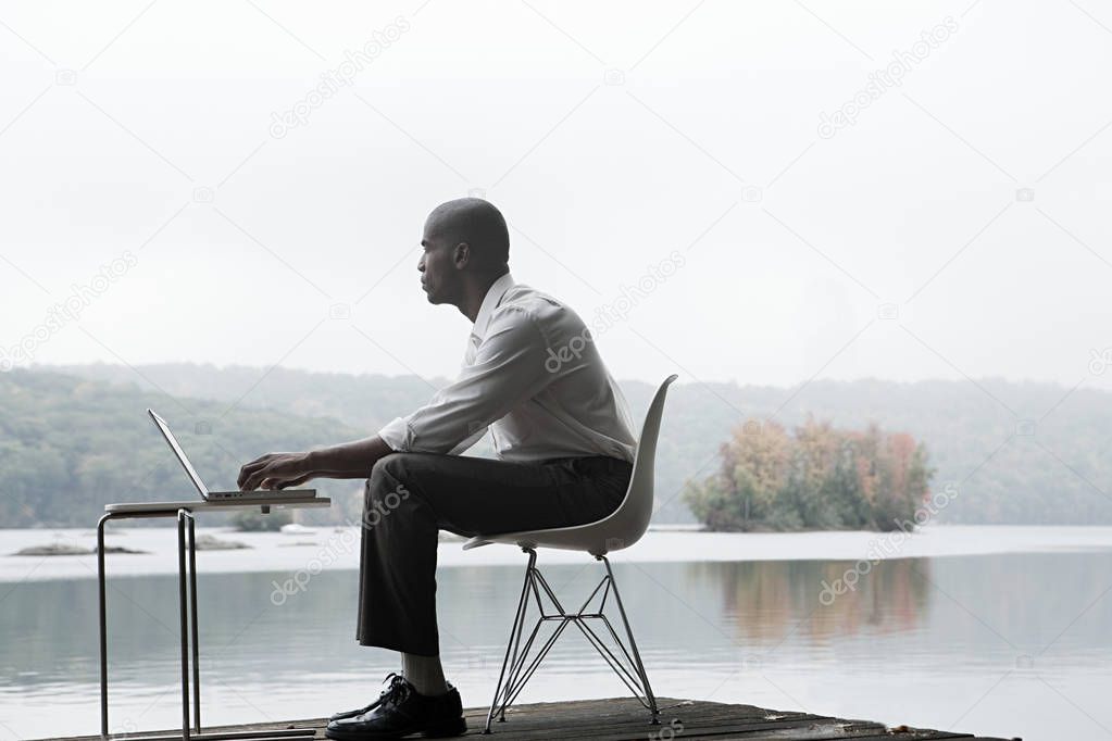 successful african american businessman using laptop in front of lake
