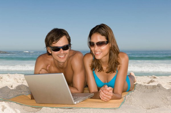 Couple using laptop on the beach