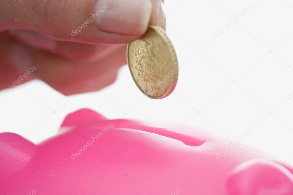 cropped close up image of female hand feeding piggy bank isolated on white