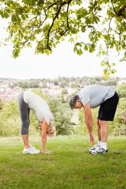 senior caucasian couple stretching and touching toes in park clipart
