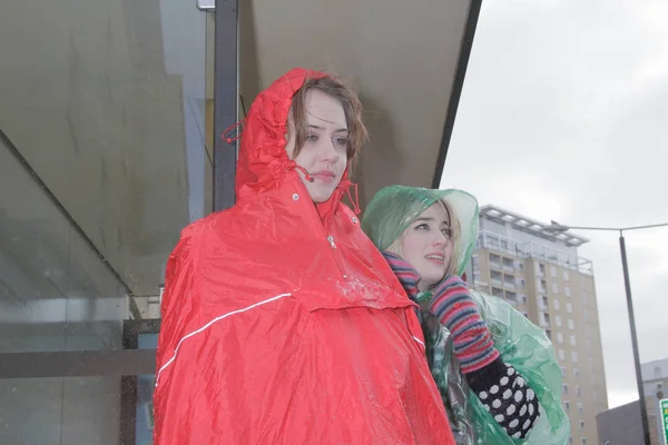 two women in raincoats at bus stop