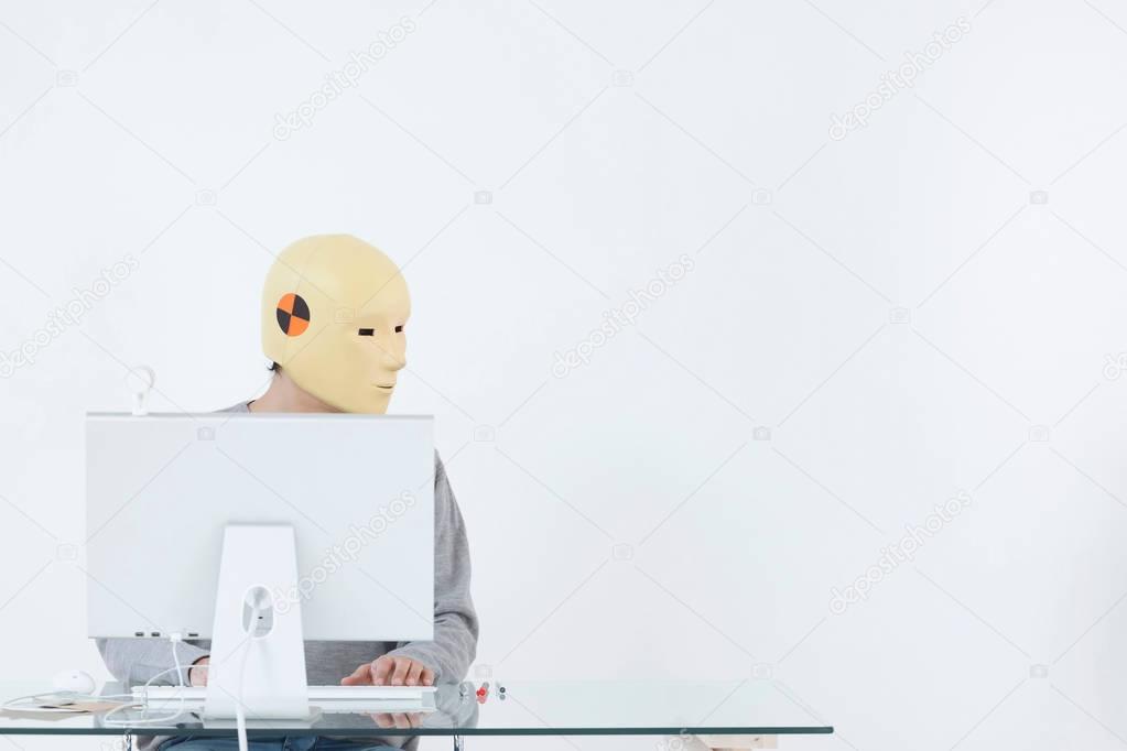 mid adult caucasian man in crash dummy mask working at computer