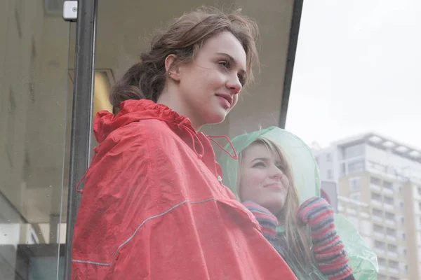 two young women in raincoats at bus stop