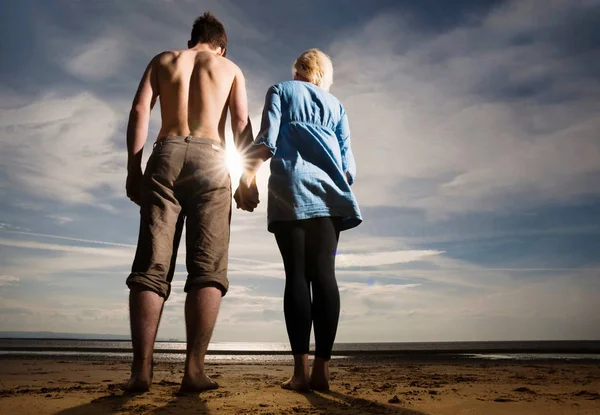 年轻漂亮的高加索夫妇牵着手在海滩上的后方视图 — 图库照片