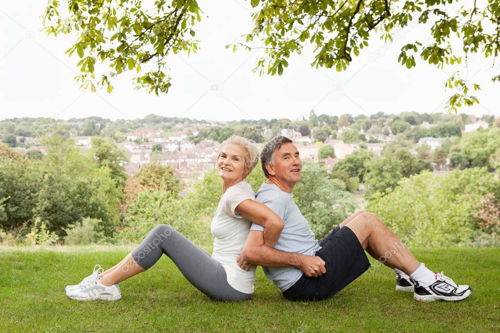 senior caucasian couple stretching back to back in park