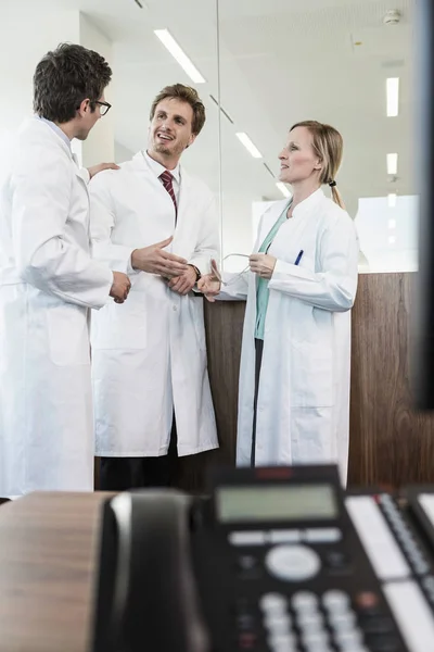 Three people wearing lab coats standing in office