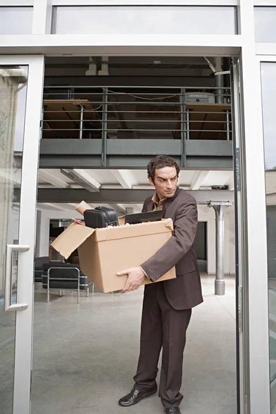 Businessman with box of belongings fired out of office