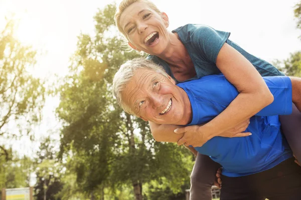 Senior Man Carrying Mature Woman Back Outdoors Laughing — Stock Photo, Image