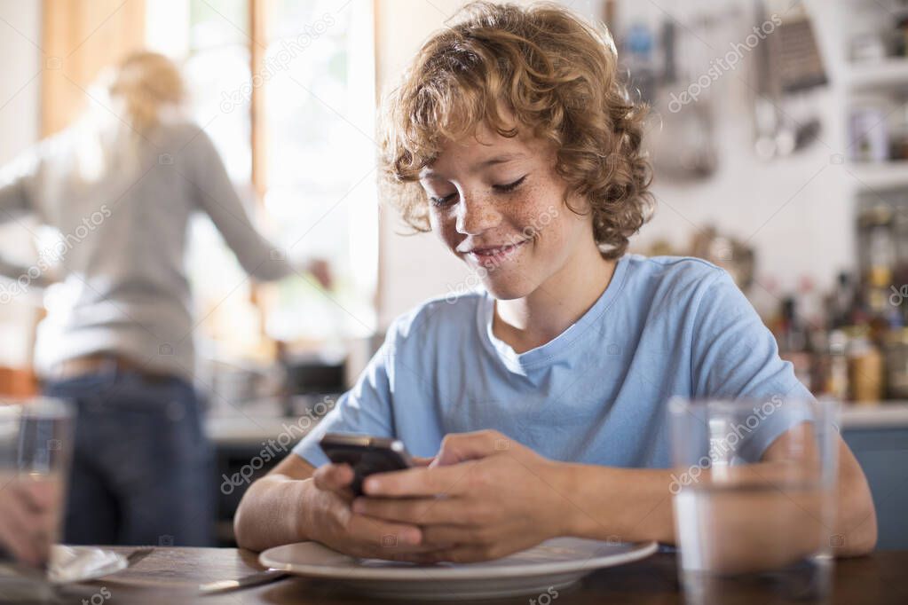 Teenage boy using smartphone at dining table