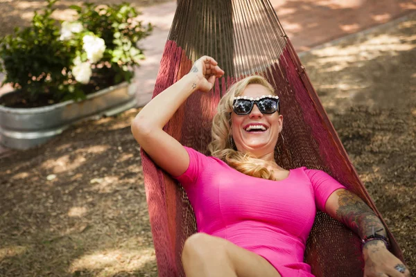 Mid adult woman with arm tattoo lying in garden hammock laughing