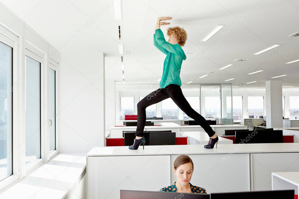 Businesswoman standing on filing cabinet, stretching and touching ceiling