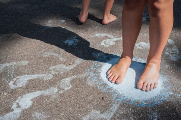 歩道でチョークの足跡を作る姉妹の裸の足 — ストック写真