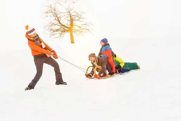 女は男と二人の男の子と雪の中でトボガンを引っ張る — ストック写真