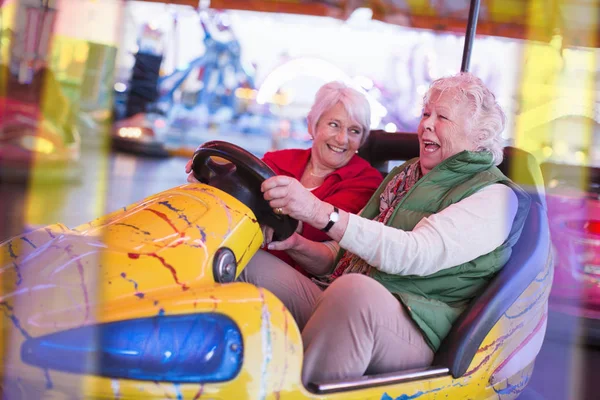 Two senior women driving bumper car at fairground