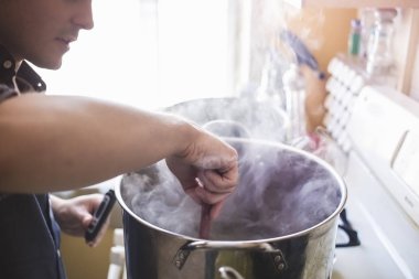 Mid adult man stirring home brew beer in pan clipart