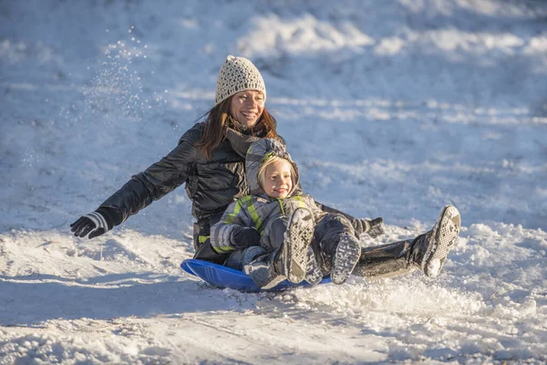 笑着的母亲和儿子在雪地里滑下坡的画像 — 图库照片