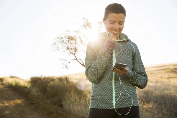 阳光下山丘上的成熟女跑步者选择智能手机音乐 — 图库照片