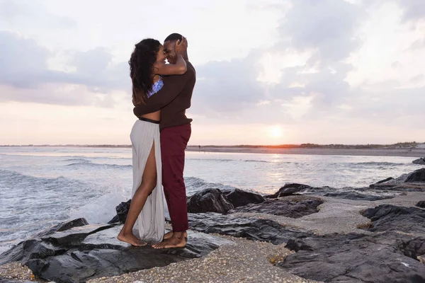 Casal de pé sobre pedras ao lado do mar, abraçando, face a face — Fotografia de Stock