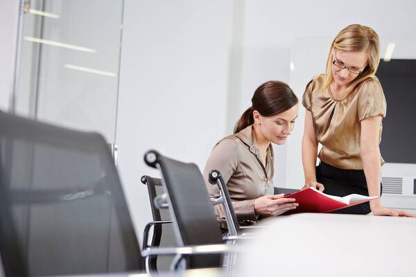 Businesswomen sitting at conference table looking at book