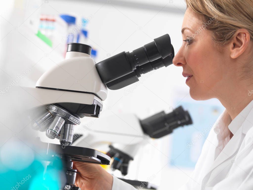 Female microbiologist viewing specimen under microscope in lab