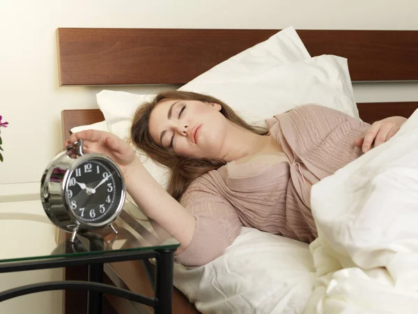 Sleepy young woman switching off alarm clock from bed