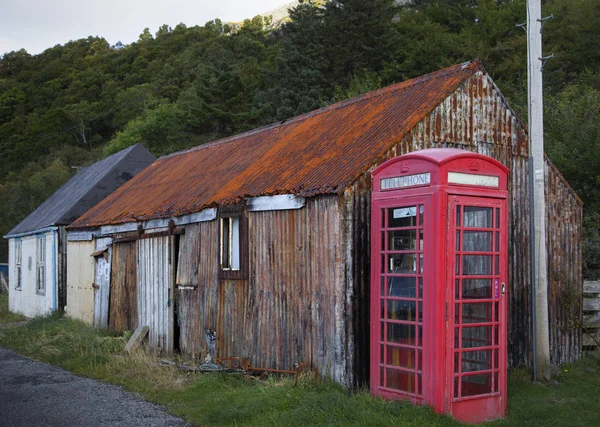 Cabine telefônica pública vermelha tradicional contra rusted dilapidated edifício de ferro ondulado, Highland, Escócia — Fotografia de Stock