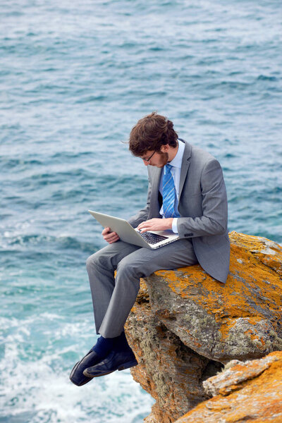 Businessman using laptop on cliff